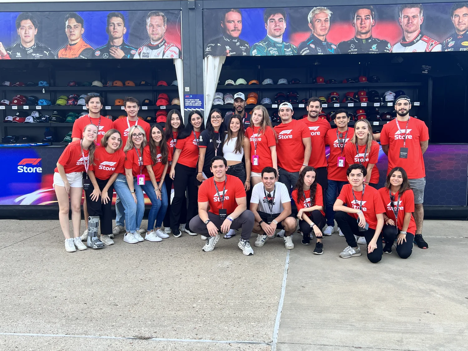 Equipo de más de veinte personas de la F1 Store en circuito, delante del expositor de gorras oficiales